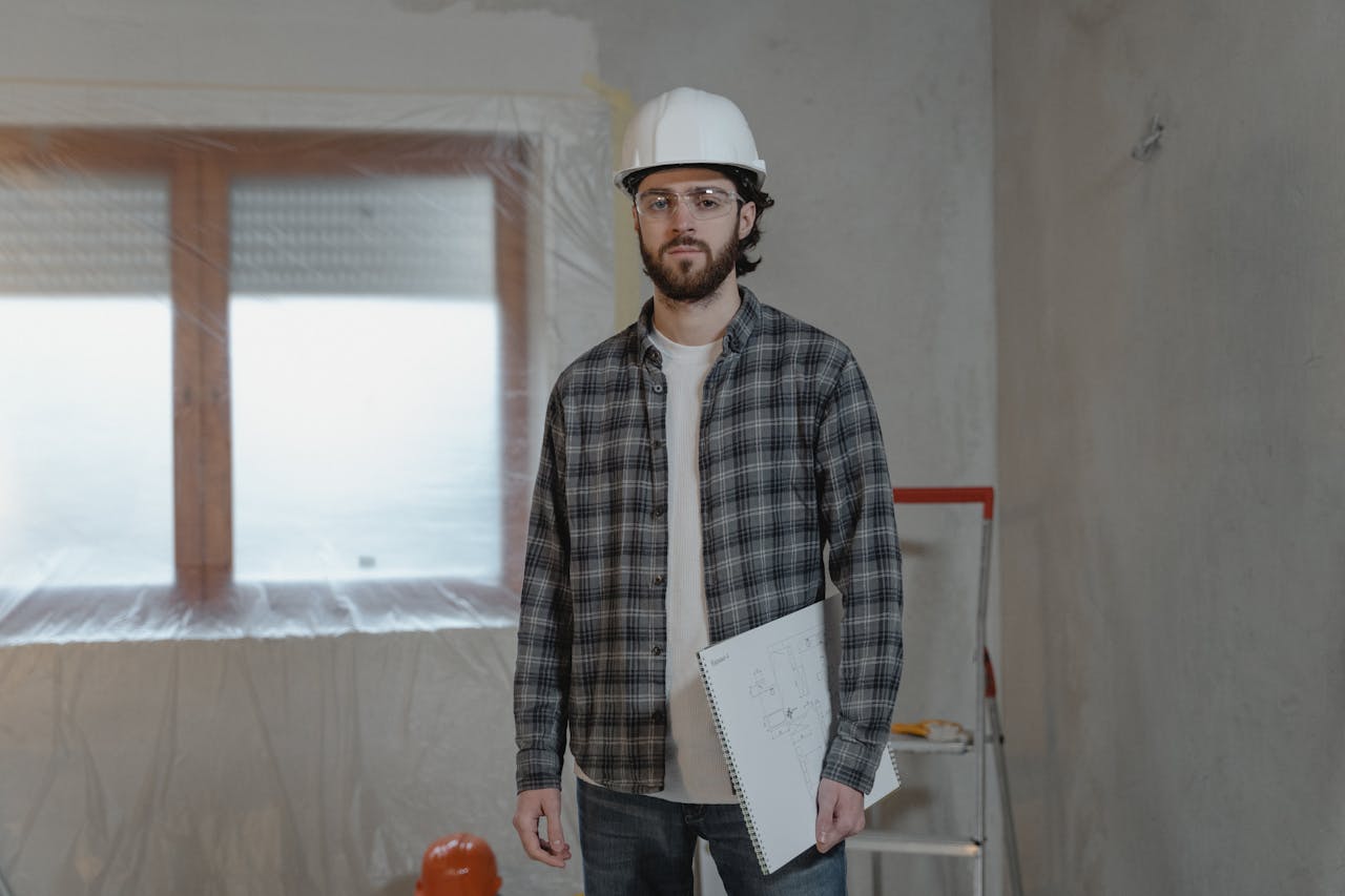 Adult male construction worker holding blueprints in an indoor renovation site.